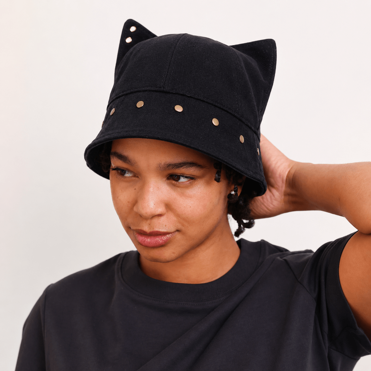 Model wearing a black cat ear bucket hat with raised ears and metal studs around the brim.