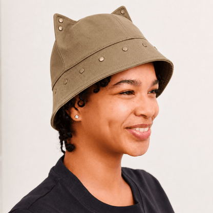 Model wearing a brown cat ear bucket hat with pointed 3D ears and subtle metal stud accents.