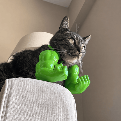 Cat wearing a green Buff Cat muscle arms photo prop with oversized biceps while leaning over the edge of a chair.