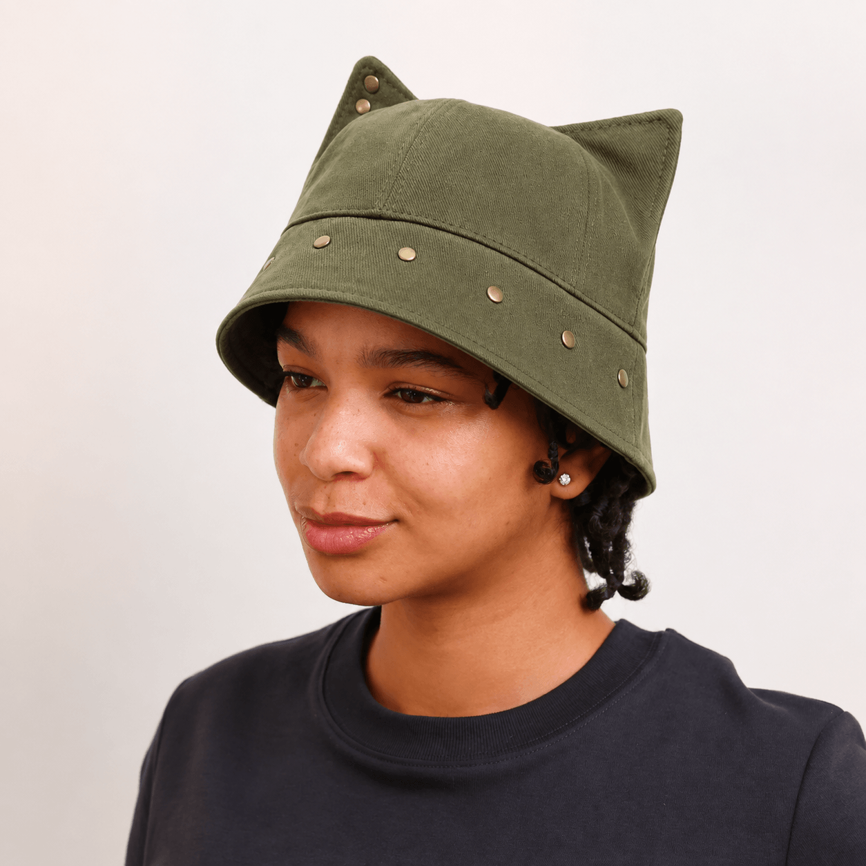 Model wearing an olive green cat ear bucket hat with sculpted ears and studded brim detailing.