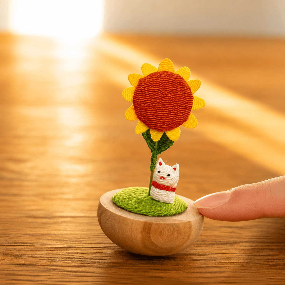A finger gently rocks the Japanese Handmade Sunflower Cat Ornament to show its self-righting wooden base.